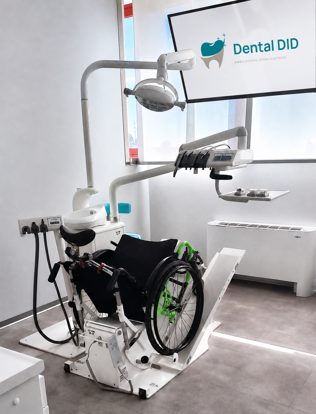Sala odontoiatrica attrezzata per l'accessibilità, con carrozzina posizionata sul riunito e schermo Dental DID sullo sfondo